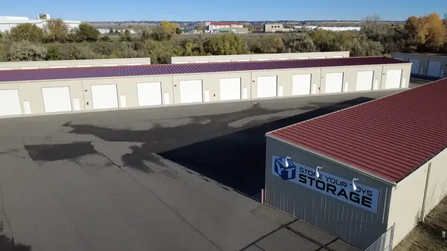 Aerial view of SYT Storage in Billings, MT: the Store Your Toys Storage sign on a red-roofed steel building, with rows of enclosed units with overhead doors behind it